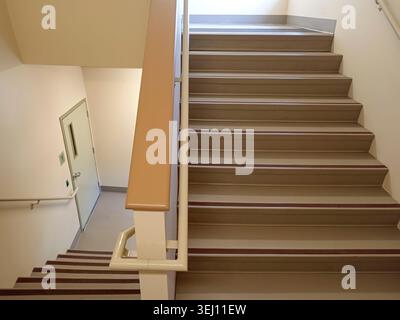 The stairwell shows safety handrails for an emergency exit in a nursing home building in Canada. The stairs lead to an exit door. Stock Photo