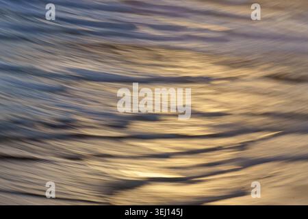 Blues and golden light and water with sweeping texture created using intentional camera movement over sea at sunset at Ripiro Beach  in Northland New Stock Photo