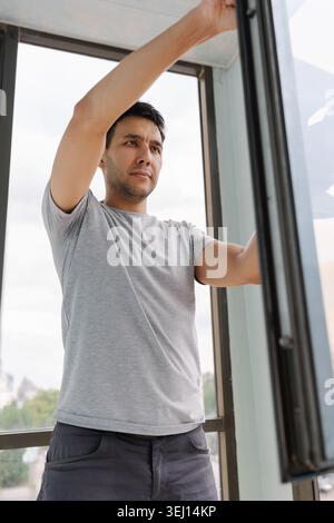 Low-angle view of young man washing window using squeegee and detergent, ensuring spotless and streak-free finish in residential home setting. Stock Photo