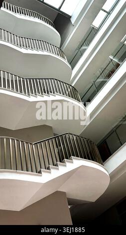 Modern architectural staircase with curved white steps and metal railings, showcasing a contemporary design in a well-lit interior space Stock Photo