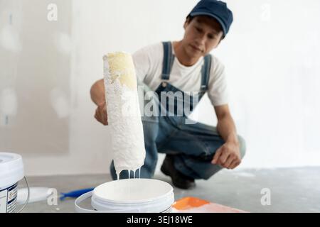 painter man, brush in hand dip on paint for restore and paint the wall, indoor the building site of a house, wall during painting, renovation, paintin Stock Photo