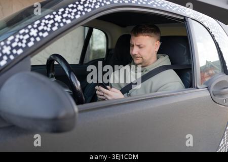 Driver using smartphone while wearing seatbelt in parked car Stock Photo