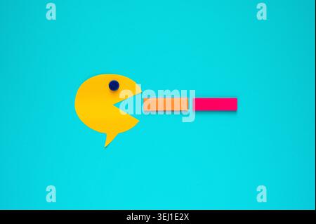 A yellow note pad in speech bubble shape eating orange and pink that are another shape of note pad on a blue background. Stock Photo