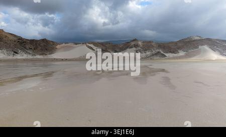 Wide sandy desert plain with pale dunes and rocky hills under dark storm clouds, creating a quiet dramatic landscape with open space and natural textu Stock Photo
