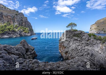 Peaceful coastal view with a sailboat floating on clear blue water surrounded by steep rocky cliffs near Sa Calobra on Mallorca west coast Stock Photo