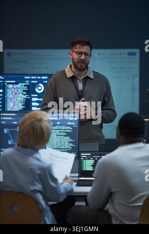 Vertical shot of Caucasian young adult man leading software team meeting, presenting coding workflow to colleagues in office. Ideal for cybersecurity, IT training, agile development Stock Photo