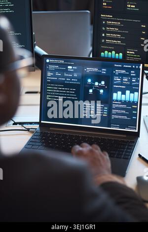 Vertical shot of middle aged professional monitoring cybersecurity dashboard and network analytics on laptop, managing IT infrastructure. Ideal for cloud security, DevOps, data protection Stock Photo