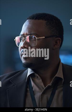 Vertical shot of Black middle aged businessman wearing eyeglasses, looking away with focused expression during corporate event. Suitable for leadership, strategy, executive branding Stock Photo