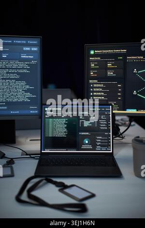 Close up of laptop and monitors displaying network security dashboards, coding and system analytics in IT workspace. Supporting cybersecurity, data protection, SOC marketing Stock Photo