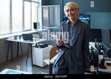 Portrait of Caucasian businesswoman holding tablet and smiling in office, presenting leadership and digital workflow. Ideal for corporate communication, management, consulting Stock Photo