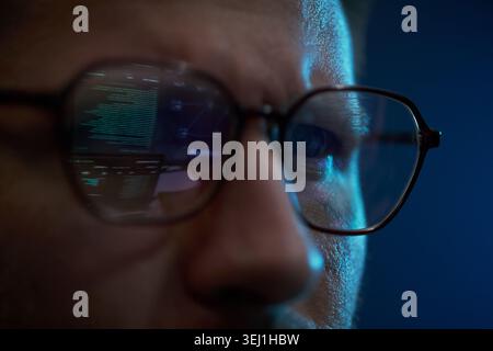 Close up of Caucasian young adult man analyzing code reflected in eyeglasses, focusing on cybersecurity work. Ideal for software development, data protection, tech marketing Stock Photo