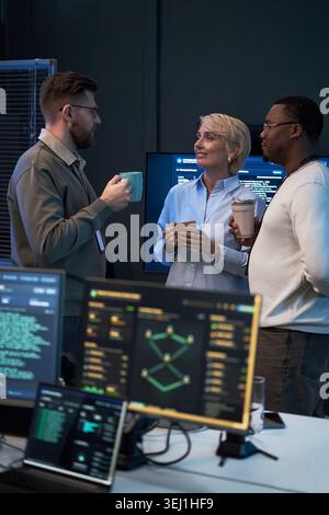 Vertical shot of diverse coworkers discussing software project during coffee break in tech office. Team collaboration and workplace communication concept for IT company marketing Stock Photo