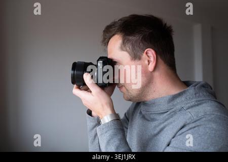 Focused man looking through the viewfinder of a mirrorless camera indoor Stock Photo