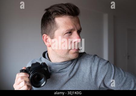Portrait of a focused man with a digital mirrorless camera looking to the side. Stock Photo