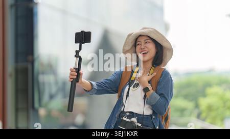 Asian woman vlogging with smartphone on selfie stick for travel content Stock Photo