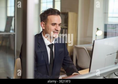 Smiling businessman at computer in office working on financial analysis tasks Stock Photo