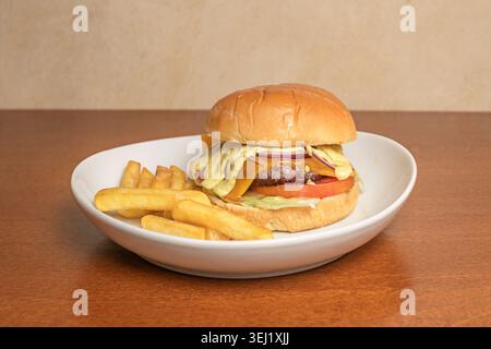 A bird's-eye view of a burger served on a dark wooden platter, the meat dripping with smoked provolone cheese, heirloom tomato slices, and curly icebe Stock Photo
