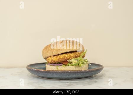 A crispy chicken burger rests on a rustic wooden board, topped with slices of dill pickle, thinly sliced ​​red onion, and a sprinkle of sweet paprika, Stock Photo