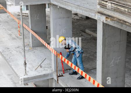 Architect in hard hat and safety glasses checking concrete column using an angle level and tablet at a building site Stock Photo