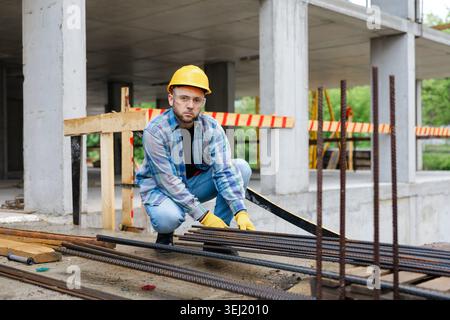 Worker in hard hat and safety glasses checking reinforcing steel bars, focusing on safety and construction development Stock Photo