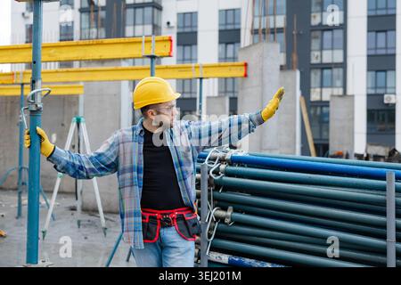 Construction worker in hard hat and safety glasses supervising building site development, extending arm measuring or indicating Stock Photo