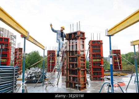 Construction worker in hard hat and safety glasses climbing ladder, setting metal formwork for a reinforced concrete column Stock Photo