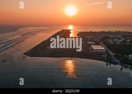 Aerial view of the airport runway and hangars on the island during a vibrant sunset with golden light reflecting on the ocean Kudahuvadhoo, Dhaalu Ato Stock Photo