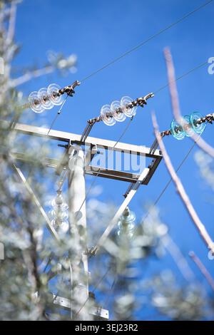 Insulators face sky. Diagonal wires cross bright blue backdrop Stock Photo