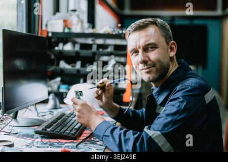 Portrait Electrician male worker happy smile working fix circuit board in workshop with Solder iron Stock Photo