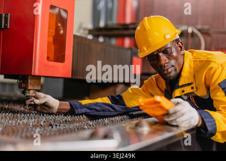 Professional African black engineer male technician expert worker control operate machine in metal plant workshop factory with safety uniform. Stock Photo