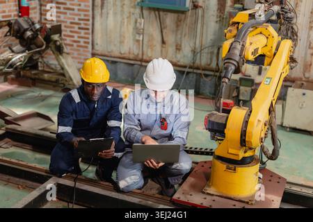 Professional engineer workers team working in metal workshop talking and working together fixing service maintenance robot machine. Stock Photo