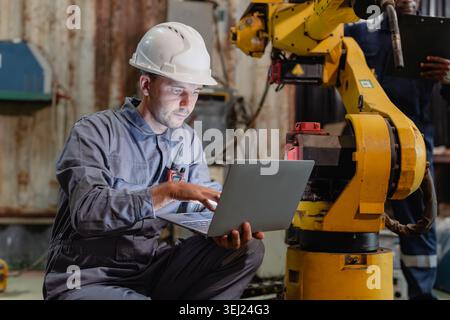Professional robotic engineer male, Technician worker using laptop computer to program, setup, check robot welder arm in metal workshop. Stock Photo