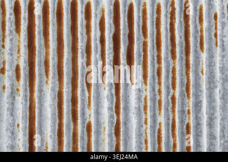 Weathered metal sheet shows vertical ridges and rust streaks. Gray surface contrasts with rich, uneven brown corrosion. Texture industrial. Background Stock Photo
