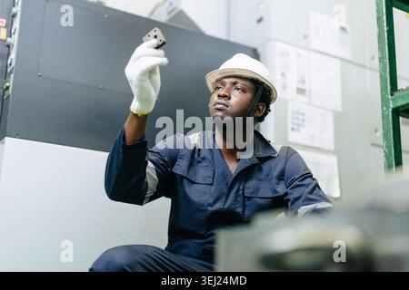 Young African black male worker in safety dress hardhat gazed at workpiece with a focused and determined , Working diligently to produce perfect, high Stock Photo