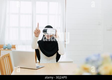 Young Muslim Asian woman using modern technology VR visual headset hand motion touching in the air play game at home Stock Photo