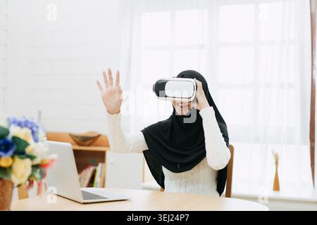 Young Muslim Asian woman using modern technology VR visual headset hand motion touching in the air play game at home Stock Photo