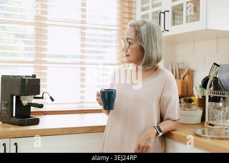 Senior Asian woman standing hand holding coffee cup, Elder drinks tea or coffee in the morning. Stock Photo