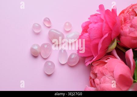 Beautiful rose quartz stones and peony flowers on a pink background. Rose quartz crystals, healing crystals. Stock Photo