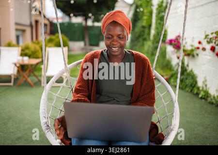 Smiling woman working on laptop in swing chair Stock Photo