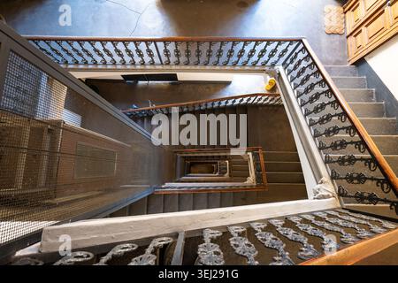 A dramatic top-down architectural perspective looking down a multi-story historic staircase, highlighting geometric lines, decorative railings, stone Stock Photo