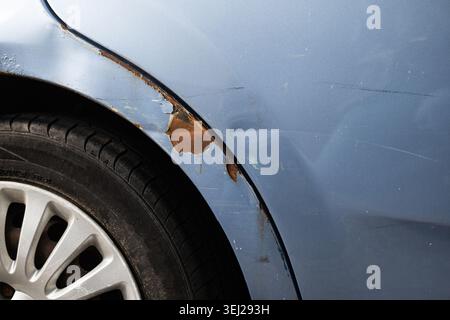 A detailed perspective focusing on bubbling, peeling paintwork and heavy brown surface rust damage on the metal fender panel of an old blue car requir Stock Photo