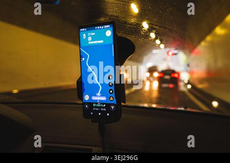 A close-up focus on a car-mounted smartphone displaying a GPS navigation route through the Axenstrasse area, with the blurred tunnel road visible in t Stock Photo
