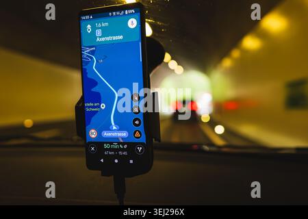 A close-up focus on a car-mounted smartphone displaying a GPS navigation route through the Axenstrasse area, with the blurred tunnel road visible in t Stock Photo