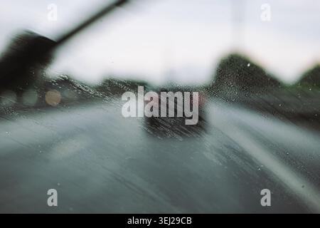 A close-up view from inside a vehicle looking through a smearing wet windshield covered in small water droplets with a wiper blade moving fast in moti Stock Photo