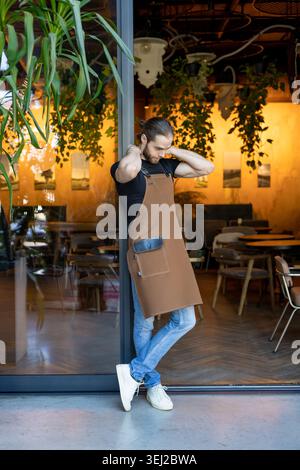 Full length portrait of man in apron fixing hair Stock Photo