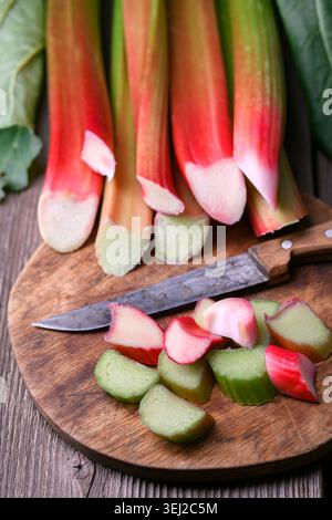 Vertical composition of rhubarb stalks and sliced pieces on cutting board, dark wood background. Raw organic rhubarb close view, natural cooking preparation Stock Photo