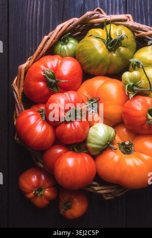 Vertical flat lay of tomatoes in basket on dark wooden background. Organic harvest concept, healthy food composition Stock Photo