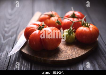 Heirloom tomatoes on round wooden board with knife. Rustic farm produce, natural organic harvest Stock Photo