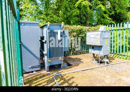 An outdoor electrical substation enclosure featuring industrial power distribution equipment surrounded by a security fence Stock Photo