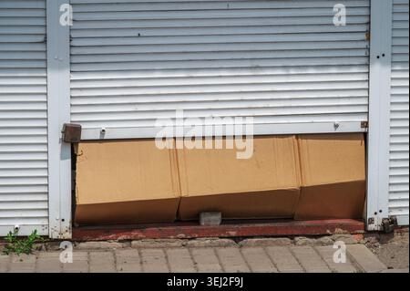 Cardboard boxes blocking partially opened metal shop shutter entrance Stock Photo